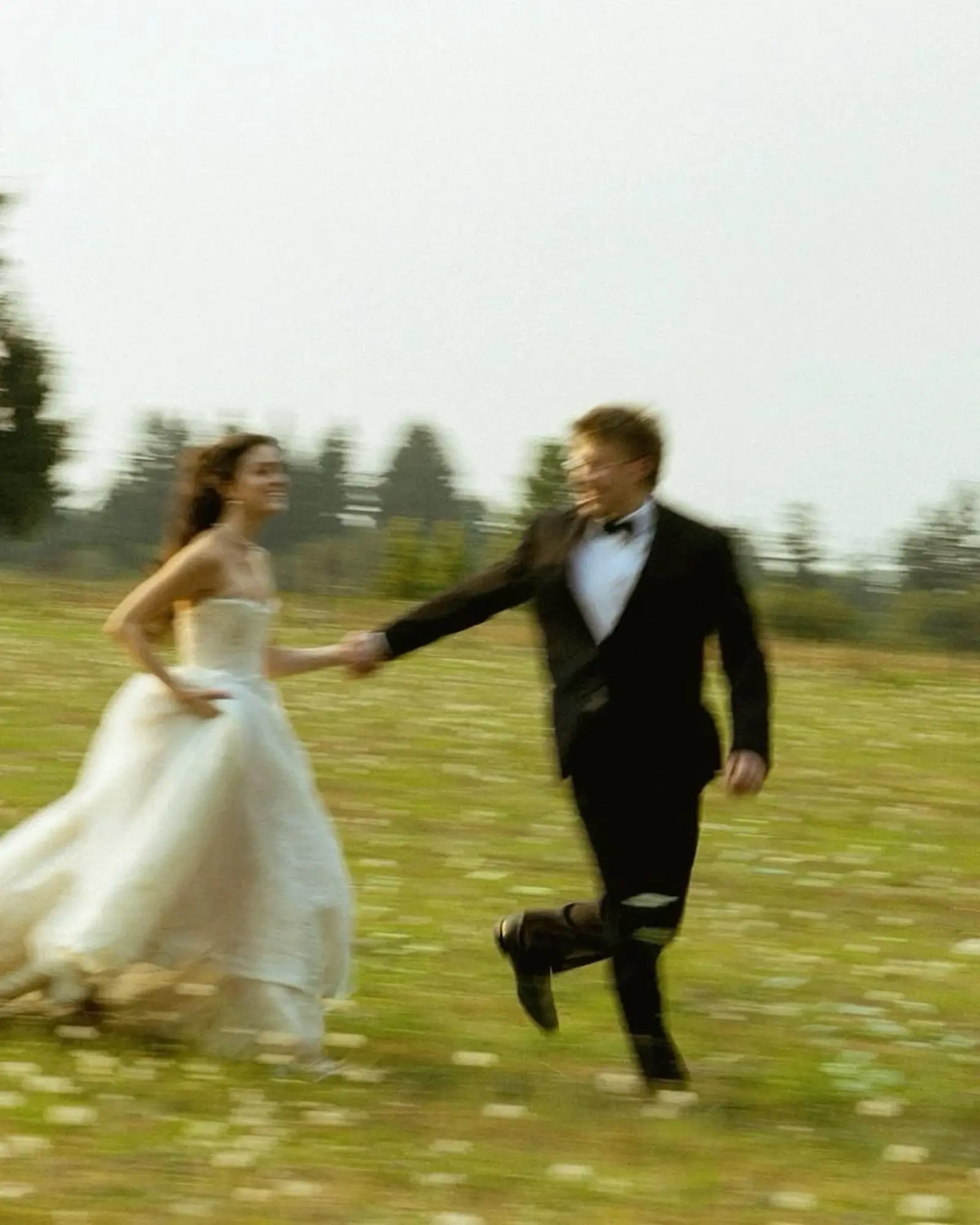 Mariés qui courent main dans la main dans un champ, la mariée en robe de tulle, photo au flou de mouvement
